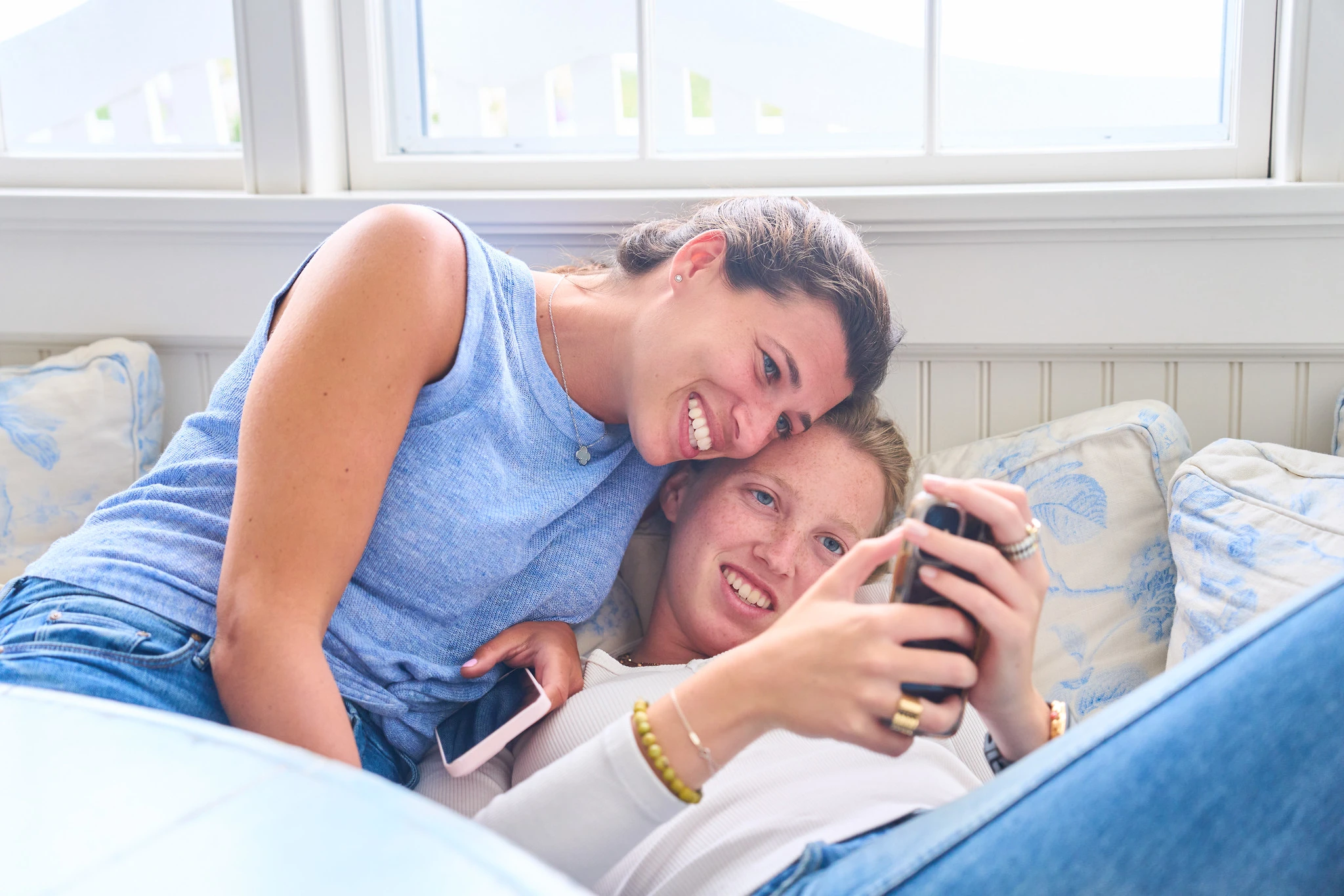 Two women sharing a smile over a phone on the sofa